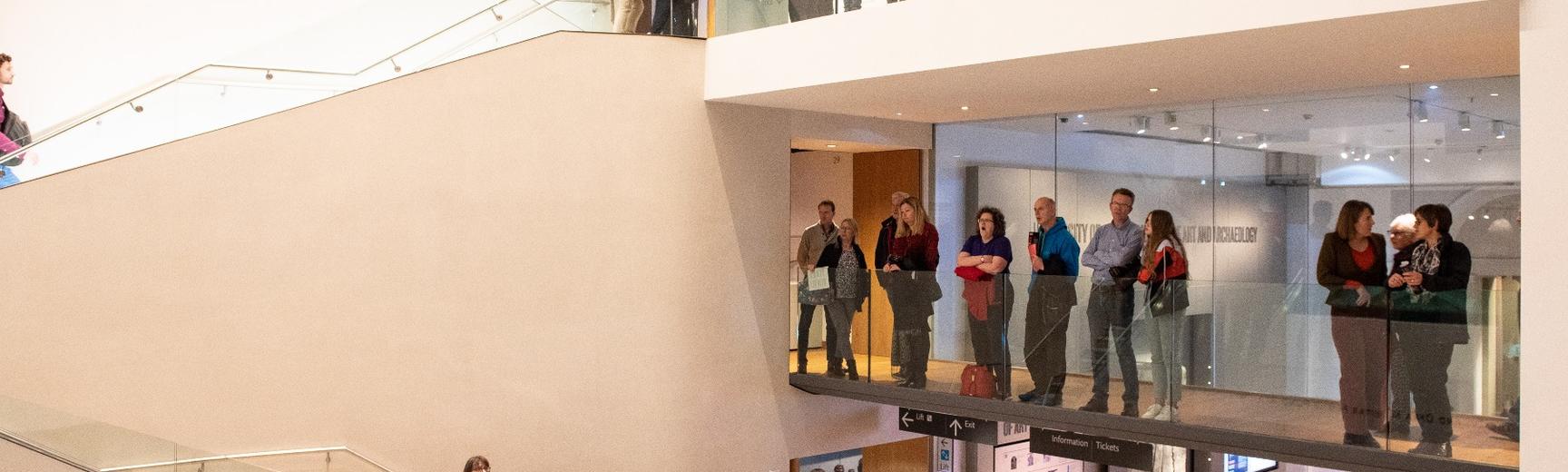 People standing on a balcony at the Ashmolean Museum viewing an exhibition that is out of frame