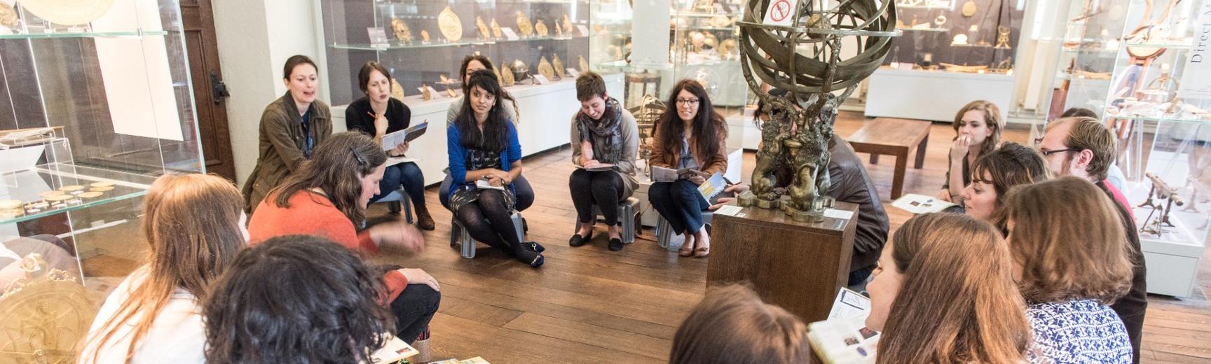 A group of people in a museum hold exhibition guides and sit in a circle discussing