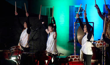 Figures playing the drums, arms above their head with drumsticks in their hands