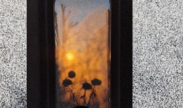 Picture of a potted plant with flowers on a window seal, with a view of a sunset, through an arched window
