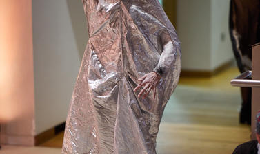 Photo of a Butoh dancer, standing and holding a silver metallic sheet over herself.