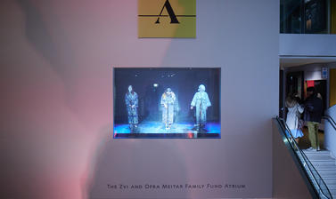 Photo of a wall with a small screen on it displaying an image of three women singing