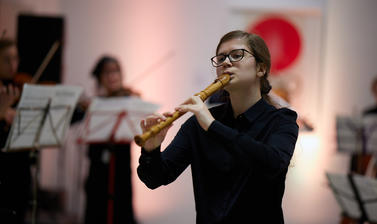 Girl playing a woodwind instrument with violinists in the background