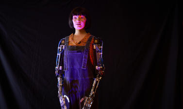 Ai-Da, a humanoid robot, visible from the knees up with visibly robotic arms.