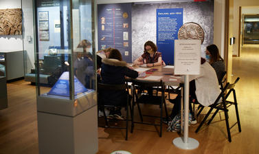 People sat around a table and writing in a museum gallery, 