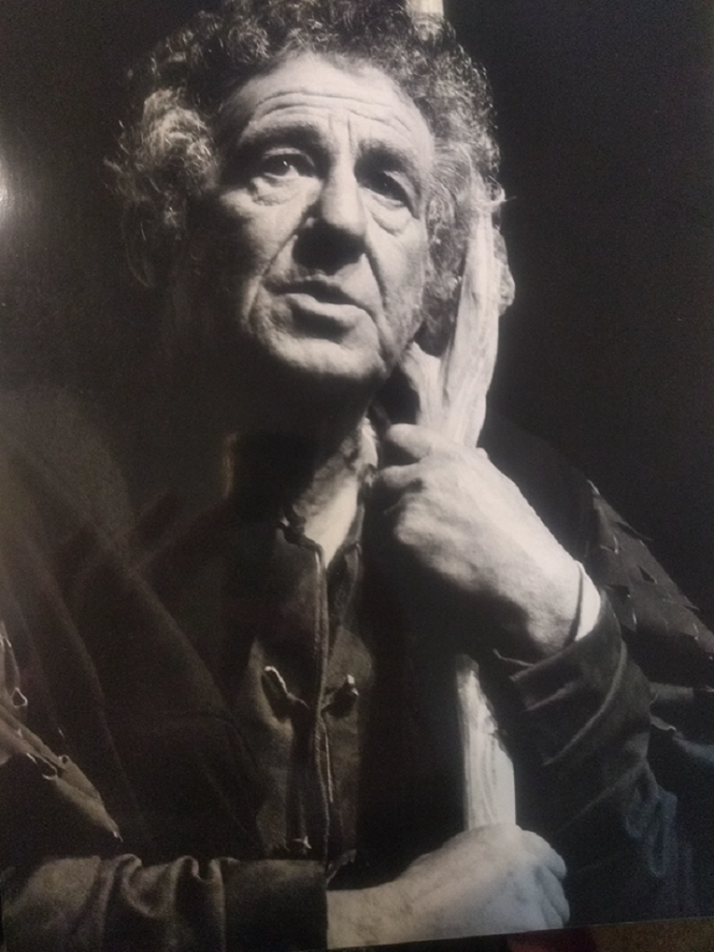 black and white photo of man leaning on staff in black coat and curly hair