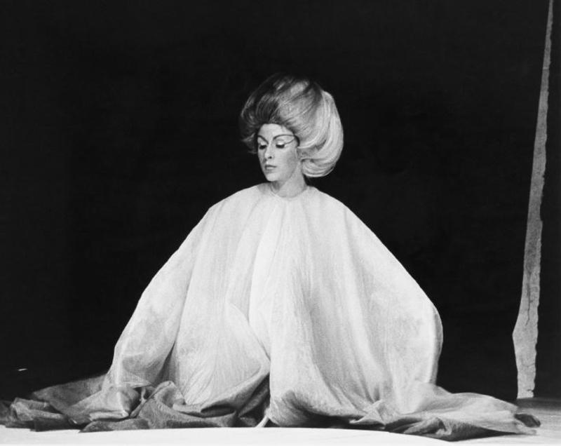 black and white image of a woman in a white costume looking like a sheet over her shoulders, hiding all form