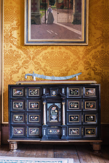 Blue decorated cabinet in front of a yellow tapestry.