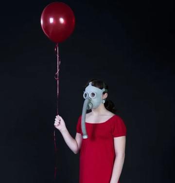 Woman in red dress and wartime gas mask holds helium red ballon