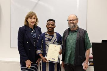three people with the middle one holding a framed certificate