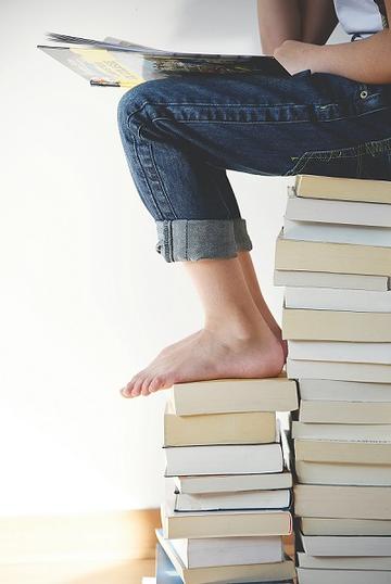 Pupil sitting on pile of books reading a book.