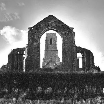 A black and white picture of the deserted church. One standing arch provides the frame for a view of the bell tower.