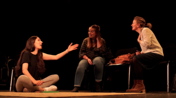 Three woman talk among themselves on stage