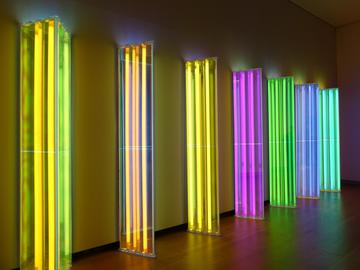 An array of vertically standing triangular prisms, made of LED lights, in a dark room. The colours vary widely.