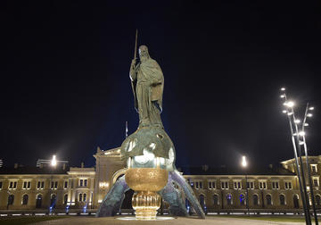 Nighttime image of bronze statue of a man standing on the top of an orb