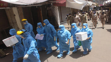 nurses in full protective gear walking thorugh a busy street