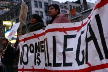 Protesters holding a sign which reads 'no-one is illegal'.