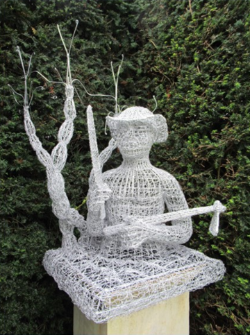 Picture of a sculpture: A human figurine (from the waist up) on a pedestal. The figurine is made of white mess, holding a sword and a mattock
