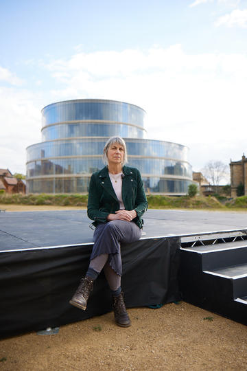 Alice Oswald sitting on a stage in front of the Blavatnik Building