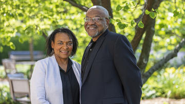 Photo of Lorna Dawes and Kwame Dawes stood smiling underneath a tree.