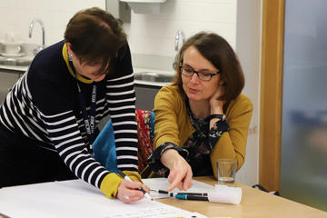 Two members of support stuff discussing and making notes on a project sheet.  