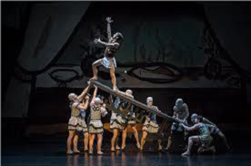 Image depicting nine ballet dancer who hold up a plank on which one ballet dancer is posed as of climbing up standing there with raised hands.