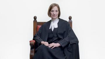 Carey Young, wearing a judge's gown, looks into the camera