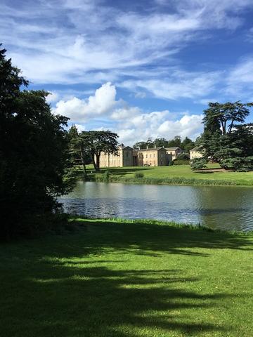 Compton Verney a grand building, sits in the background of a small river and grass banks, taken on a sunny day