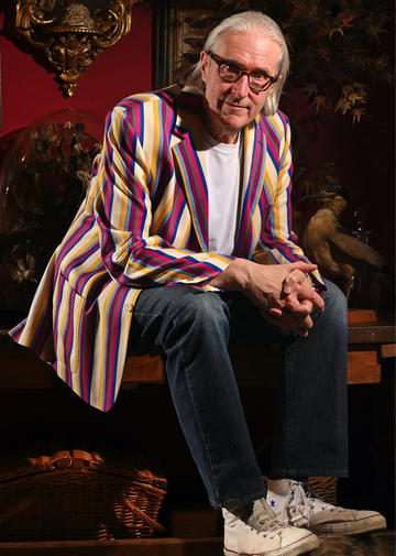 John Harle sitting in a chair leaning on his knees and wearing a striped jacket.