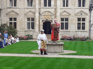 Actors in medieval costumes on St Edmund's Hall's quad, one holding the college crest