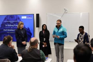 4 people standing in a line and one of them reading out to the audience