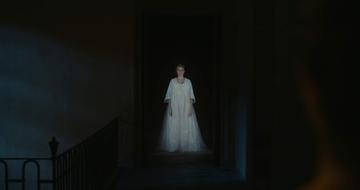 Woman dressed in Victorian white dress emerges from dark doorway