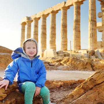 Image depicts a pupil sitting in front of the Greek temple of Poseidon at Cape Sounion.