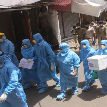 nurses in full protective gear walking thorugh a busy street