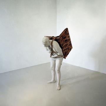 Photo of a sculpture, a figure bent over with a wooden item strapped to its back