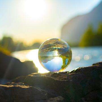 A glass ball reflecting water, trees and rocks, similar to a globe.