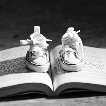 Image depicting a photograph of an open book on which a pair of kids sport shoes are placed.