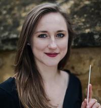 Headshot of woman smiling at camera, wearing a black top, holding a conductor stick