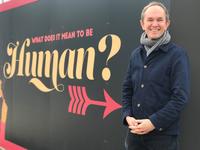 John Fulljames in front of a sign reading 'what does it mean to be human?'