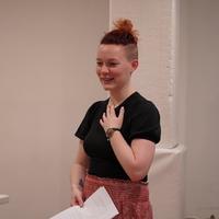 woman stands up in black top and maroon trousers