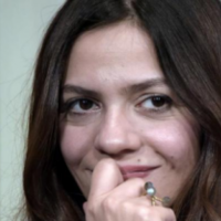 head shot of woman with brown hair, hand to lips