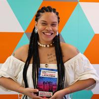 Maria Clara Araújo dos Passos holding a copy of her thesis