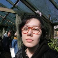 man in black sweatshirt with black hair and red framed glasses