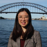 women in grey jacket smiling in front of a bridge and waterway
