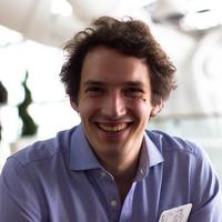 Jeremias Adams-Prassl smiling at the camera with brown hair and a blue shirt against a blurred background