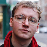 blond man with red scarf over black top, gold rimmed glasses