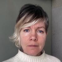 headshot of a woman with brown and blond hair looking at the camera wearing a white turtleneck