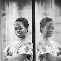 Black and white image with woman leaning against glass in floral dress, reflected on the glass