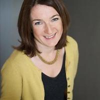 Abigail Williams smiles at the camera in a yellow cardigan against a dark blurred background