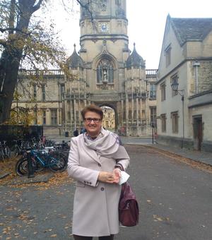 woman in tan trench coat standing in front of a college at Oxford